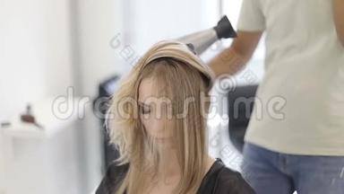 一位男理发师在一家现代化的美容店里烘干长发、金发、吹风机。
